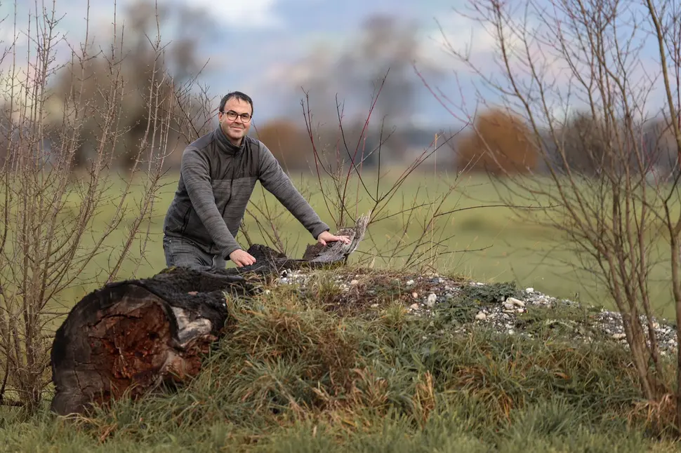 Foto von Heinz Biedermann, der in einer Wiese vor einem toten Baumstamm steht und in die Kamera lächelt